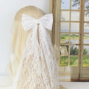 White lace bow hair clip with bridal mesh veil shown on model for wedding hairstyles