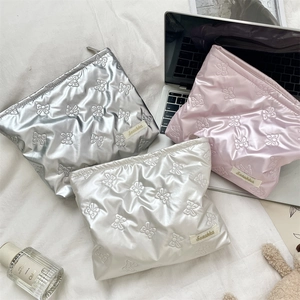 Detailed top view of quilted bow-pattern cosmetic bags in silver, pink, and pearl white