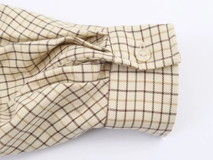 Macro shot of plaid shirt cuff featuring beige check pattern and a white button detail