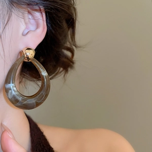Detail view of model wearing brown marble resin teardrop earrings with gold stud details