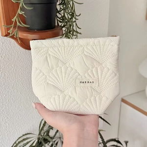 Close-up of cream quilted cosmetic bag featuring gold zipper and shell pattern texture