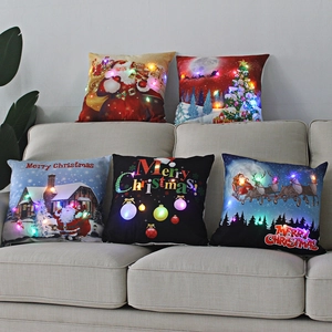 Five LED Christmas throw pillows with festive prints on a soft beige sofa set