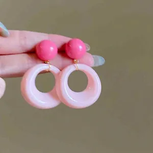 Vue détaillée des boucles d'oreilles en acrylique rose avec détails dorés en main