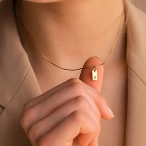 Close-up detail of a gold-plated stainless steel rectangular pendant with letter R