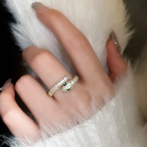 Detailed view of a gold snake ring with white cubic zirconia and green gem eyes on a hand