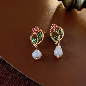 Vintage gold hollow rose earrings with a white teardrop pearl on leather background
