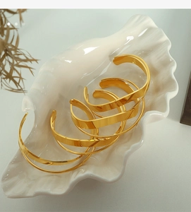 Set of five minimalist gold polished open bangles displayed on a white shell tray