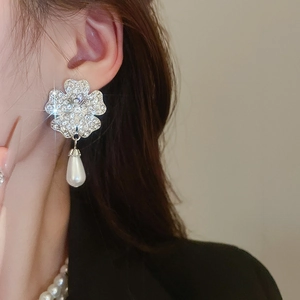 Close-up of silver clover earrings with sparkling rhinestones and drop pearl charm