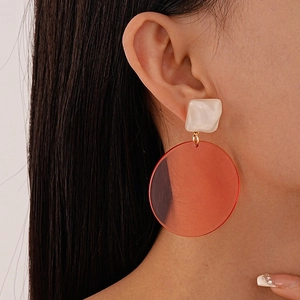 Close-up of minimalist resin earrings featuring white square studs and translucent orange drops