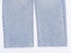 Détail du tissu denim bleu clair avec embellissements en perles blanches et ourlet brut
