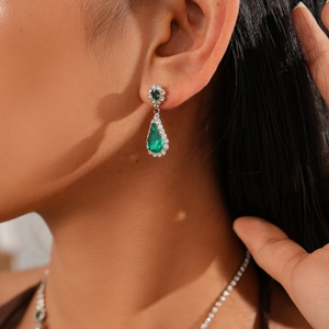 Detailed close-up of vintage silver earrings with green teardrop crystal and halo diamonds