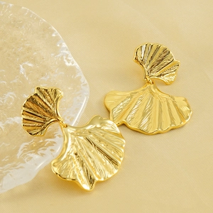 Golden ginkgo leaf earrings with detailed vein textures on minimalist beige fabric background