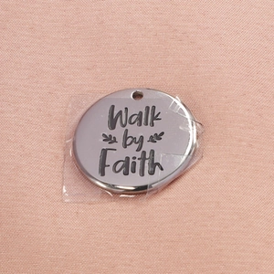 Polished stainless steel round pendant engraved with Walk by Faith on pink fabric