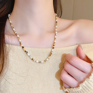Detail of freshwater pearl and agate beaded necklace with gold metal cubes on skin