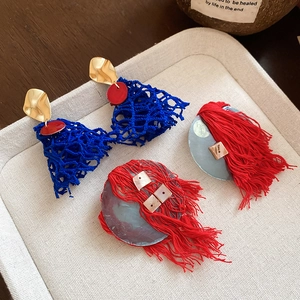 Detail of artistic earrings featuring blue crochet net and long vibrant red fabric tassels