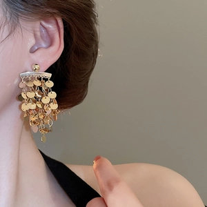 Detailed view of tiered gold circular sequin tassel earrings worn by a fashion model
