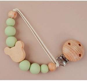 Detail of wooden bear pacifier clip with mint green silicone beads on pink background
