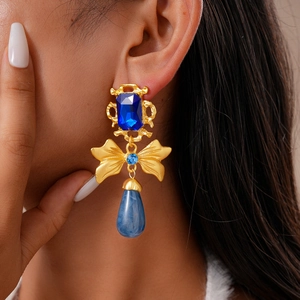 Detail of vintage gold bow earrings with blue rhinestones and marble teardrop pendant