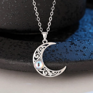 Macro shot of silver crescent moon pendant with intricate filigree and glowing gemstone