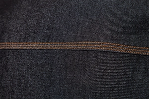 Détail macro du denim bleu foncé avec double couture orange contrastée sur chemise