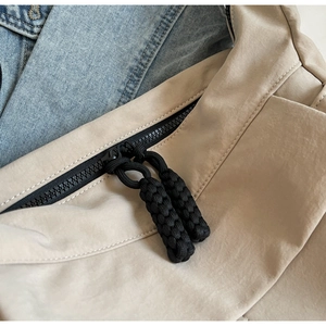 Close-up of the smooth dual zippers with black woven pulls on a beige nylon tote bag