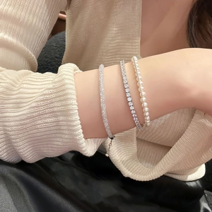Detail of layered jewelry set with silver tennis bracelet, pearl beads and zircon cuff