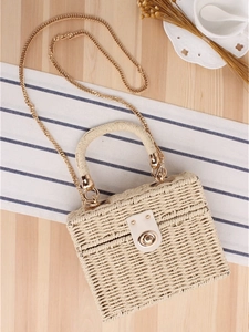 Beige woven box bag with gold chain strap on a wooden table with rustic decor