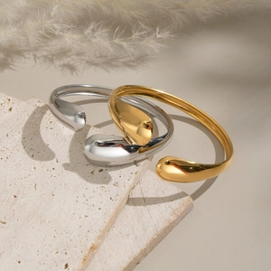 Minimalist teardrop open bangle in gold and silver finish on artistic stone background
