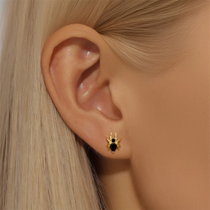 Macro detail of a gold spider stud earring with black crystals worn on an ear
