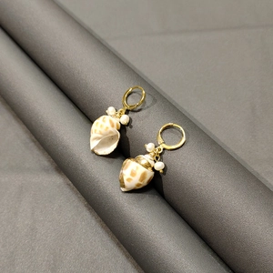 Detail view of golden shell earrings featuring natural mother of pearl and white pearls