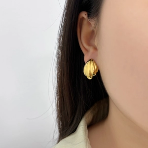 Close-up of a 18K gold shell-shaped stainless steel stud earring on a female model