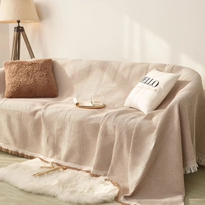 Beige waffle weave sofa throw cover with decorative tassels in a cozy home setting