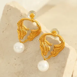 Golden leaf-shaped pearl earrings with brushed texture on natural stone background
