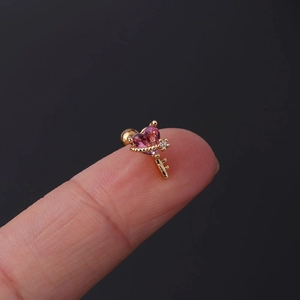 Macro shot of a tiny gold key cartilage earring with pink heart stone on a fingertip