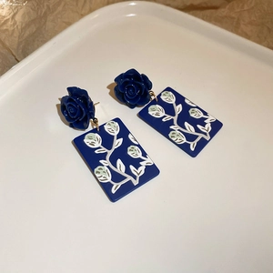 Detailaufnahme dunkelblauer Rosenohrringe mit künstlerischem Sonnenblumenanhänger auf Tablett