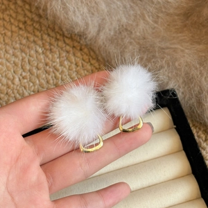 Detailed shot of white faux fur pompom earrings with golden geometric hardware accents