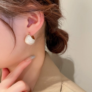 Detailed close-up of a gold-plated drop earring with white enamel on a model's ear
