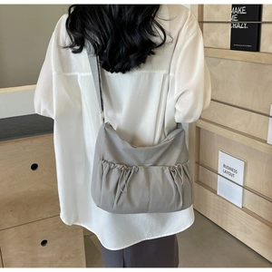 Detail of grey nylon crossbody bag with drawstring pockets on a model in a minimal setting