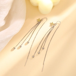 Detail of silver star tassel earrings with box chains and smooth beads on a soft fabric