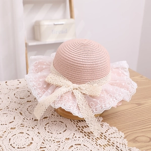 Close-up of pink straw hat featuring delicate white floral lace brim and large bow detail