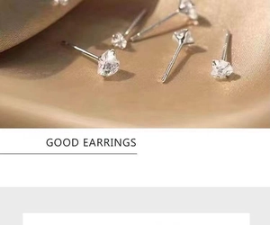 Macro shot of silver stud earrings with clear zircon on luxurious champagne silk fabric
