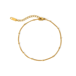 Détail d'une chaîne de cheville en acier inoxydable doré avec perles sur fond blanc pur