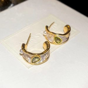 Detail of C-shaped drop earrings with green gemstone and pearl inlay on gold frame