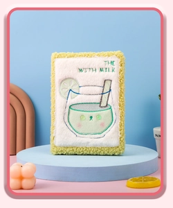 Primer plano de cuaderno de felpa con diseño de taza de leche bordada y detalles de limón