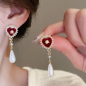 Detail of red flocked heart earring with pearl border and drop pearl on model's ear