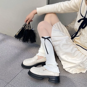 Detail of white cable knit leg warmers featuring black bows and platform loafers