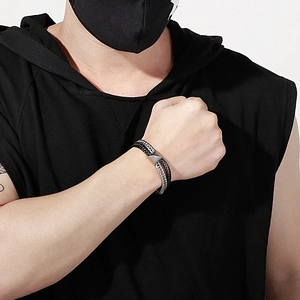 Close-up of layered stainless steel snake chain and woven leather bracelet on wrist