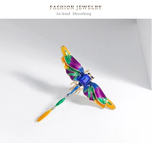 Detailed close-up of a vintage dragonfly brooch with blue stone and colorful enamel wings
