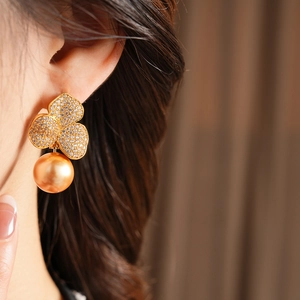 Close-up of elegant gold flower earrings with crystals and pearl drop on model ear