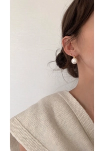 Close-up of a large white pearl earring with a gold buckle on a female model's ear